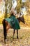 A woman in a long dress sits on a horse. Autumn forest, horse breeding