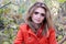 Woman with long hair in orange coat looking at camera and sitting in bushes in forest