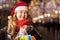 A woman with long hair and a Santa hat near the window of a city store with purchases in colorful, paper bags. New year`s shoppin
