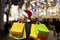 A woman with long hair and a Santa hat near the window of a city store with purchases in colorful, paper bags. New year`s shoppin