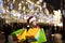 A woman with long hair and a Santa hat near the window of a city store with purchases in colorful, paper bags. New year`s shoppin