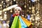 A woman with long hair and a Santa hat near the window of a city store with purchases in colorful, paper bags. New year`s shoppin