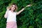 Woman with long hair in white blouse looking at camera in front of green bushes