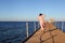 Woman in a long pink dress walking on the beach. lady in straw blue hat and pink dress walking on the wooden harbour. Vacation and