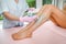 Woman with long tanned perfect legs and smooth skin having wax stripe depilation hair removal procedure on legs in beauty salon.