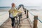 Woman looking at camera and smiling dressed in light summer clothes, sunglasses with bicycle on the wooden sea pier on sandy