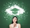 Woman looking at the cloud with graduation hat over the head. Green chalk board as a background.