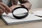 Woman looking at document through magnifier at wooden table, closeup. Searching concept