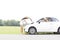 Woman looking at female friend repairing broken down car on country road