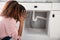 Woman Looking At Leaking Sink Pipe In Kitchen