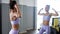 Woman is looking at mirror on her sportive beautiful body after workout in gym.