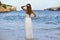 Woman looking thoughtful at sea water in summer holiday enjoying vacation relaxed wearing white beach dress