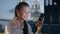 A woman looks at her phone, smiles and types a message against a backdrop of a night city and glowing buildings, work