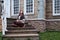 A woman looks up sitting on the porch of a retro style building