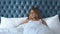 Woman lying in bed yawning, trying to relax in hotel room, noisy neighbors