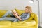 Woman lying on cozy yellow couch and reading book