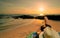 Woman lying down on sand beach at sunrise. Woman with straw hat sunbathing on tropical paradise beach with beautiful sunrise sky.