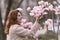 Woman magnolia flowers, surrounded by blossoming trees., hair down, wearing a light coat. Captured during spring