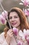 Woman magnolia flowers, surrounded by blossoming trees., hair down, wearing a light coat. Captured during spring