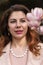 Woman magnolia flowers, surrounded by blossoming trees., hair down, wearing a light coat. Captured during spring