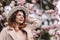 Woman magnolia flowers, surrounded by blossoming trees., hair down, white hat, wearing a light coat. Captured during