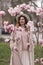 Woman magnolia flowers, surrounded by blossoming trees., hair down, white hat, wearing a light coat. Captured during