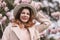 Woman magnolia flowers, surrounded by blossoming trees., hair down, white hat, wearing a light coat. Captured during