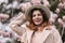 Woman magnolia flowers, surrounded by blossoming trees., hair down, white hat, wearing a light coat. Captured during