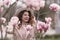 Woman magnolia flowers, surrounded by blossoming trees., hair down, white hat, wearing a light coat. Captured during