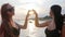 Woman make heart hands on background sea, girls looking at camera and show heart on embankment