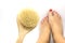 Woman makes massage legs with wooden soft massage brush for body and legs on white background. Anti cellulite home spa treatment