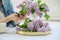 Woman making bouquet of lilac branches, close-up female arranging flowers bunch in vase