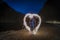 Woman making a heart shape with a sparkler at night with towering cliffs in the background o