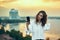 Woman making self portrait with her smart phone over cityscape golden sunset
