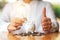 A woman making and showing thumbs up hand sign while putting light bulb over a piggy bank on the table