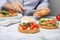 Woman making tasty rusks with different toppings at white marble table, closeup