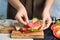 Woman making tasty sandwich with sausage at table