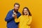 Woman and man cheerful couple with phones in hand talking on cell phone crooked smile cheerful, on yellow background