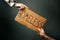 A woman and a man hold a cardboard sign with the inscription HOMELESS. Dark background. Hands close-up. The concept of