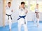 Woman and man in kimono standing in fight stance during group karate training in gym