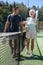 Woman and man in sportswear walking on outdoor court along net with paddle racket and ball in hands after match, talking