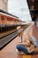 Woman in a mask on the platform near the train. The girl is sitting at the train station near the train. Travel by rail. View of a