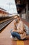 Woman in a mask on the platform near the train. The girl is sitting at the train station near the train. Travel by rail. View of a