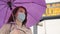 Woman in mask standing at bus stop with umbrella
