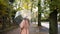 Woman in mask walks on autumn street under transparent umbrella during rain.