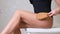 Woman massaging the skin of her legs with a dry massage brush on a white background. The girl is fighting cellulite.