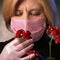 Woman in a mature age in a mask is trying to catch the smell of a flower. Keeps the flowerpot in protective gloves