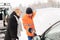 Woman mechanic looking under car hood snow