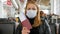 A woman in a medical mask at the airport with a passport and a plane ticket.