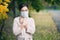 A woman in a medical mask, coat and glasses presses her hands to her chest